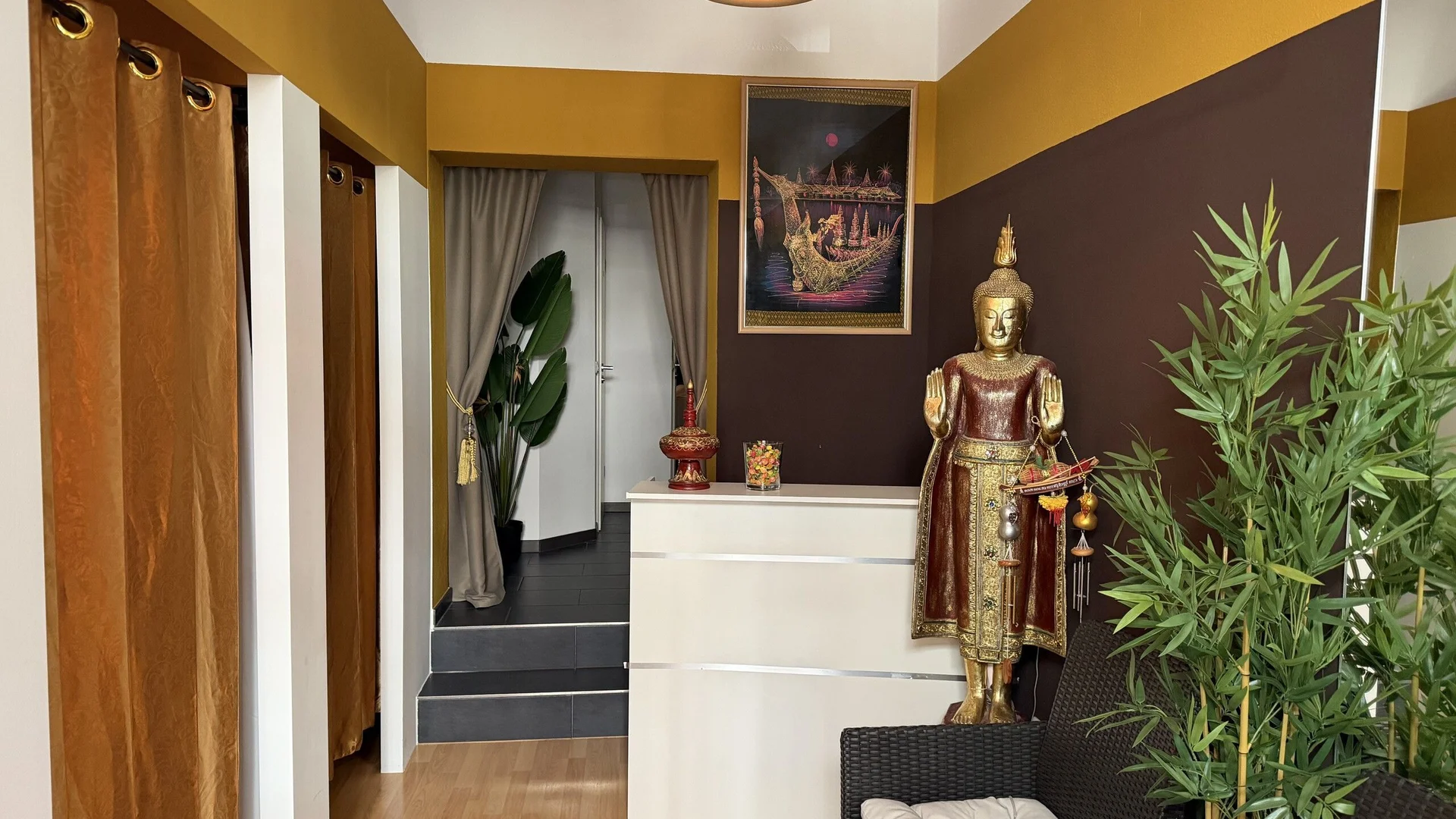 Empfangsbereich von Sala Thai Massage & Spa mit goldener Buddha-Statue, Bambus und thailändischer Kunst, Stievestraße 15, München